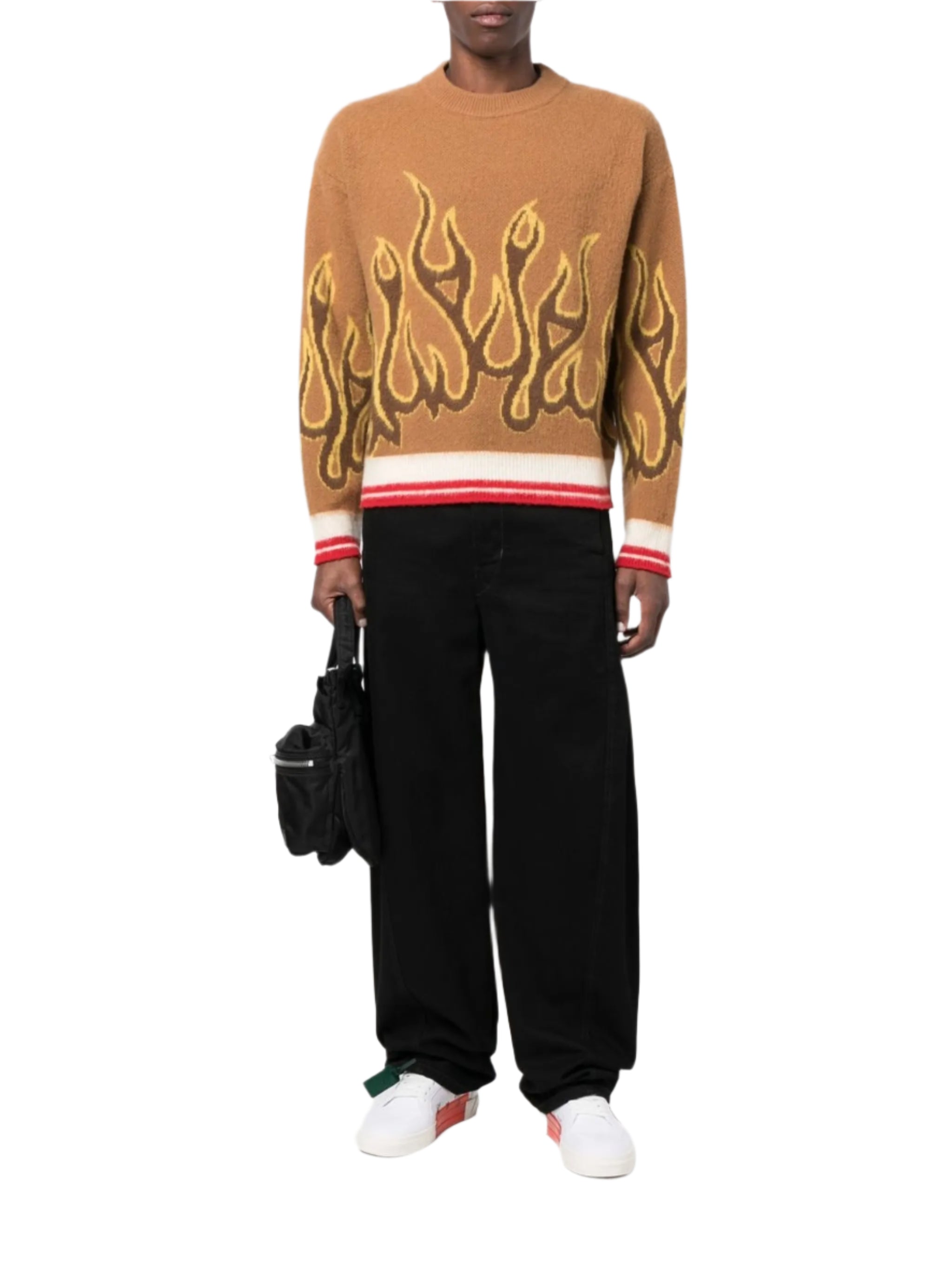Person wearing a brown sweater with flame design, black pants, and white shoes on a white background