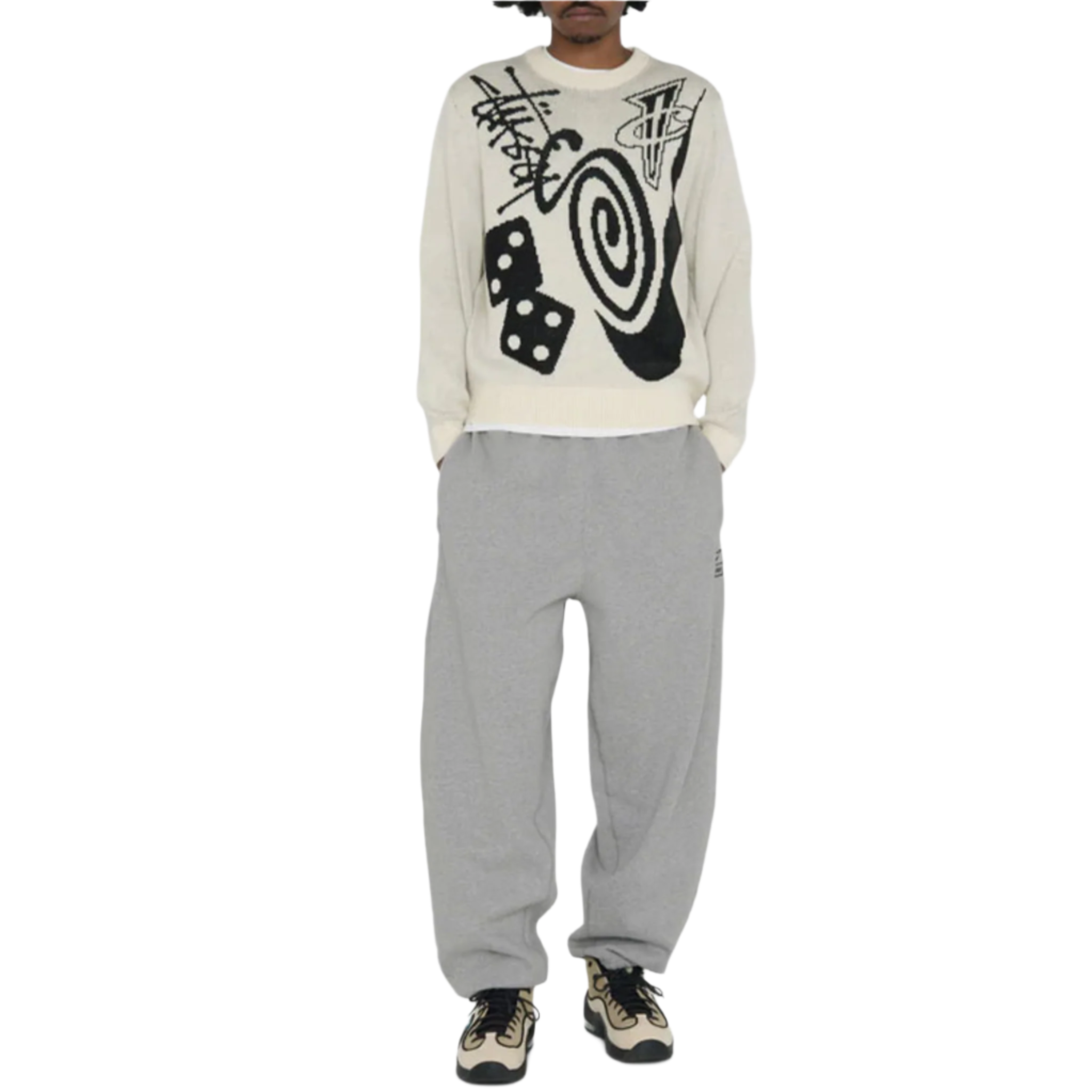 Person wearing a cream Stüssy sweater with black abstract design and gray pants on a white background